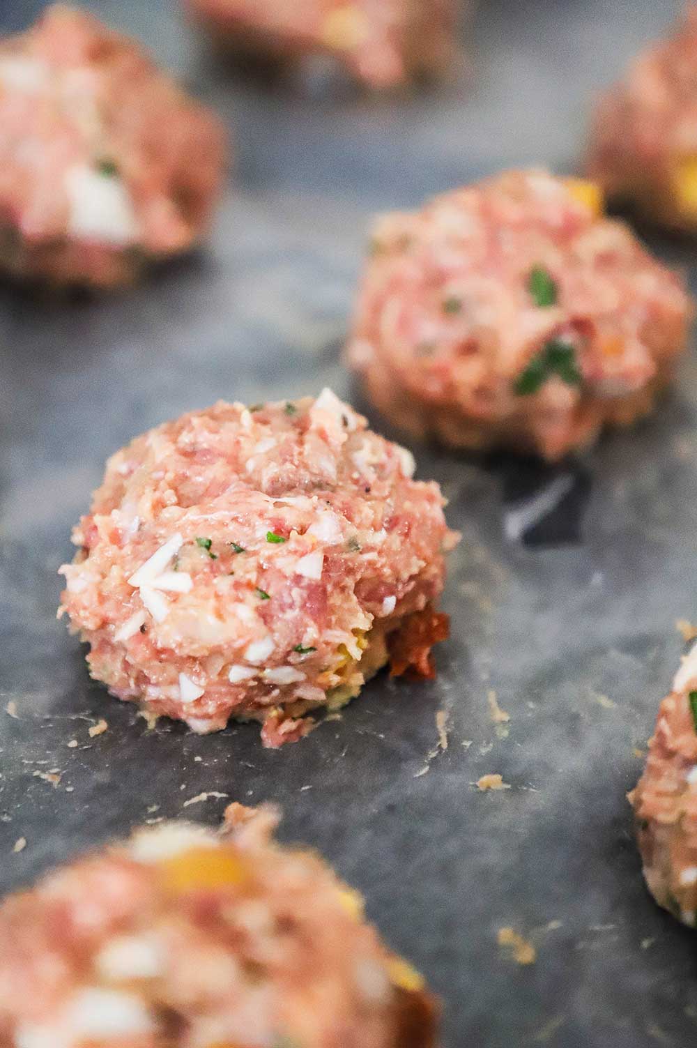 A close-up view of an uncooked albondigas Mexican meatball sitting on wax paper next to other meatballs.