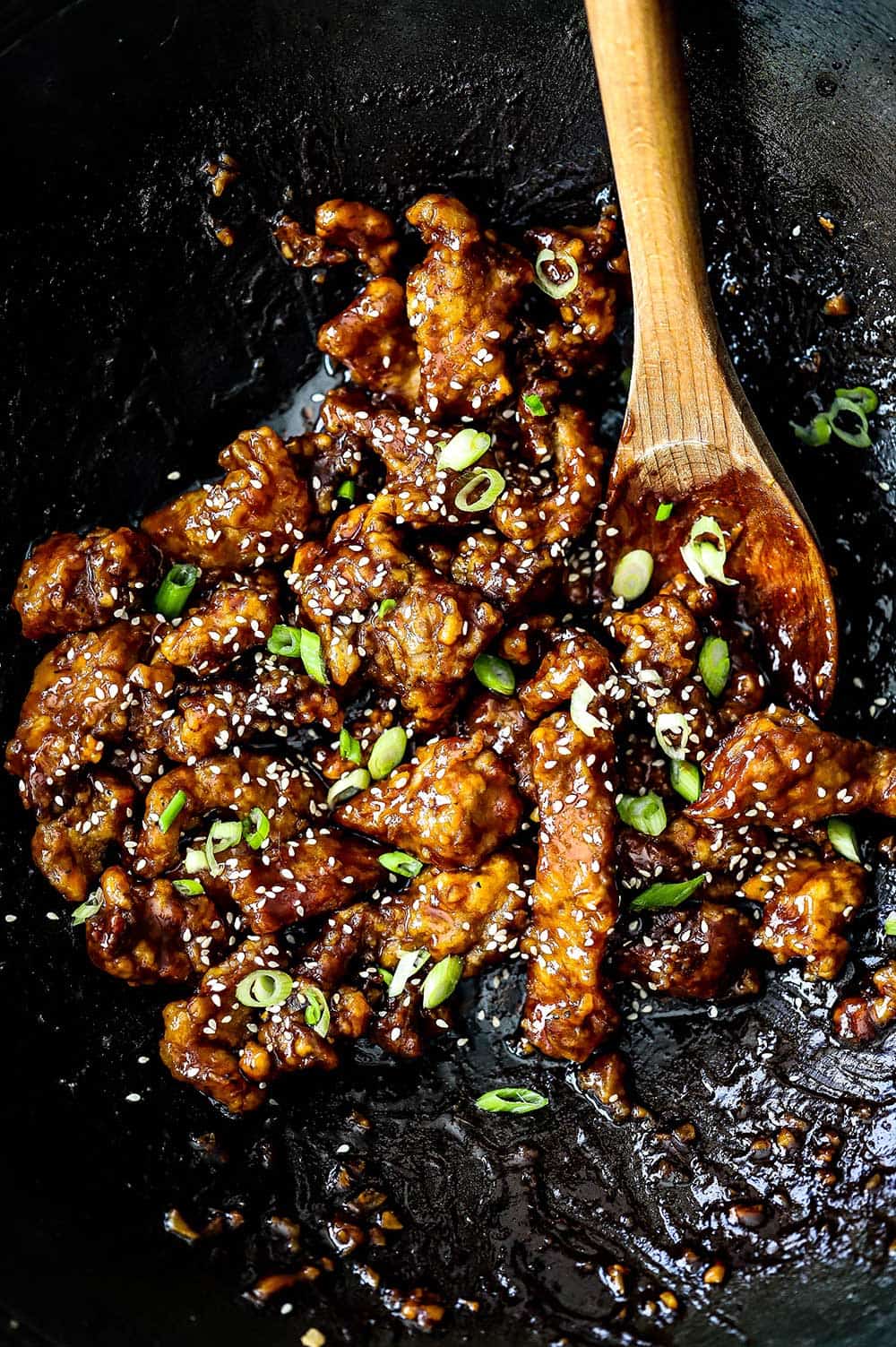 An overhead view of a wok that is filled with sesame beef and a wooden spoon off to the side.