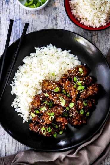 An overhead view of a dark plate that is filled with crispy sesame beef and rice.
