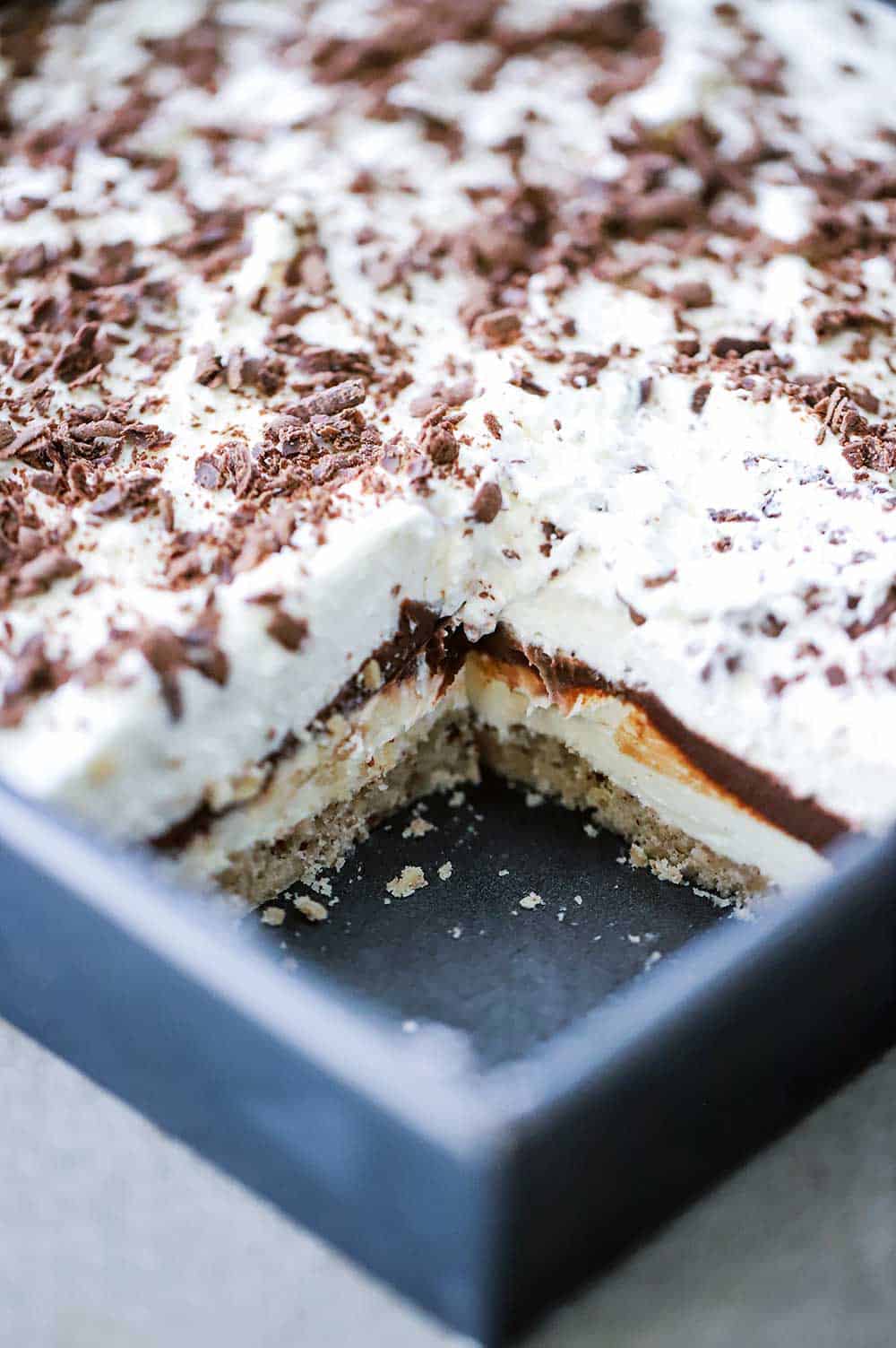 A square metal baking pan filled with a dessert that is layered with shortbread crust, cream cheese, chocolate pudding, and whipped cream.