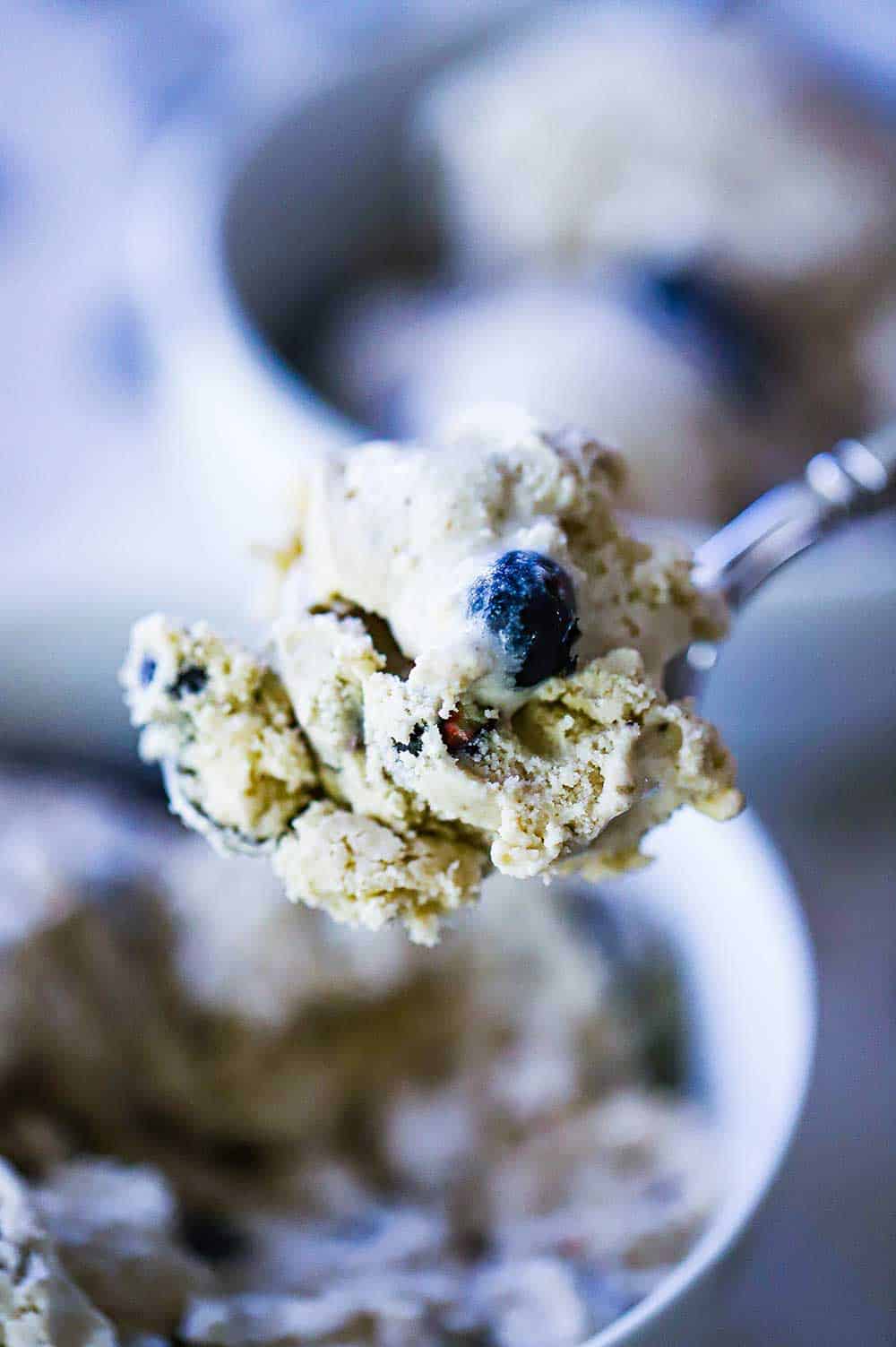 A spoon holding up a large frozen scoop of frozen blueberry ice cream.