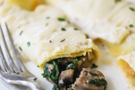 Two savory crêpes on a plate with one that has been broken open with mushrooms and spinach spilling out of it.
