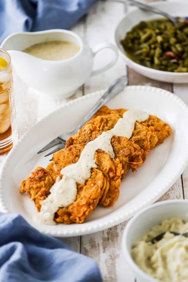 A white platter filled with five Southern-fried pork chops with cream gravy drizzled down the middle of them.