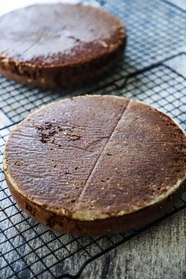 Two baked chocolate cakes sitting on baking racks and they have not been frosted yet.