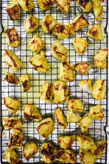 Bite-sized chunks of broiled chicken that has been marinated in a Indian yogurt sauce sitting on a baking rack.