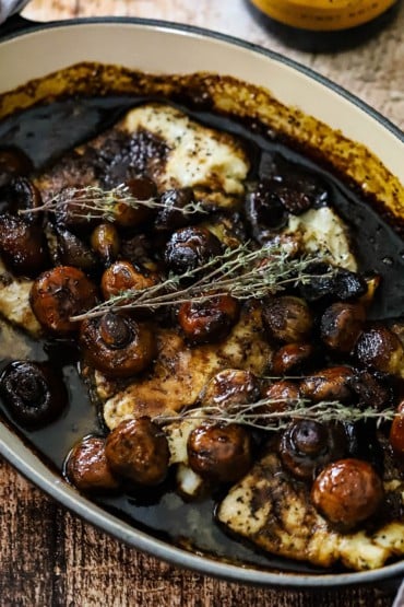 An oval baking dish filled with baked haddock fillets surrounded by and topped with a mushroom agrodolce sauce.