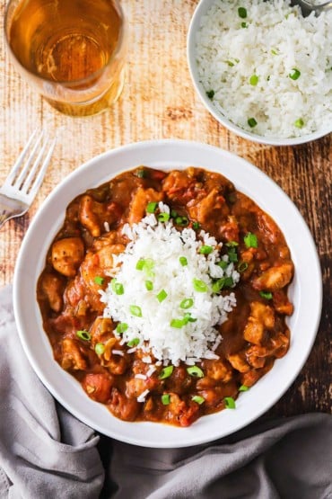 An overhead view of a bowl of creole chicken with a mound of white rice in the middle and a bowl of rice nearby.