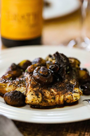A white dinner plate filled with seared haddock that is topped with sautéed mushrooms in an agrodolce sauce.
