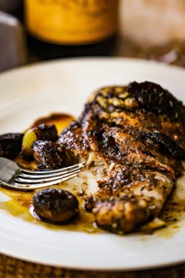 A white plate filled with a fillet of seared haddock covered with mushroom agrodolce sauce and a fork that has taken a bite out the fish.