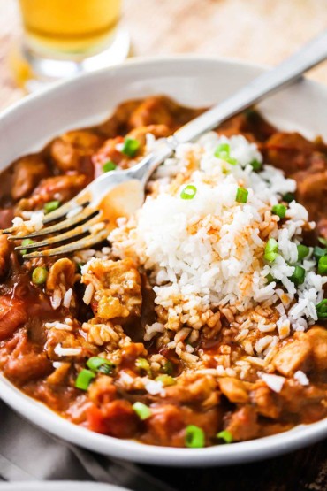 A white bowl filled with a red sauce and chunks of chicken mixed in with white rice.