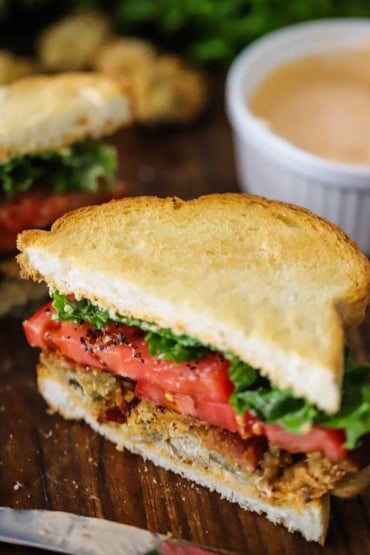 A fried oyster BLT that has been sliced in half and is sitting on a wooden cutting board.