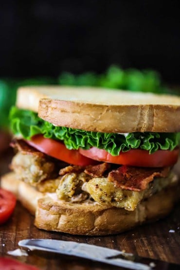 A close-up view of a sandwich filled with fried oysters, crispy bacon, sliced tomatoes, lettuce, and mayonnaise.