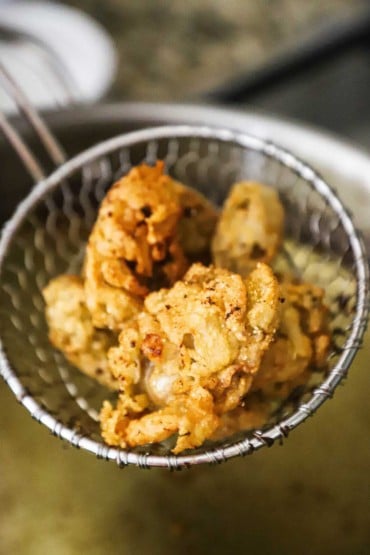 An overhead view of a kitchen spider holding several deep-fried oysters.