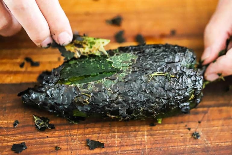 A person pulling the charred skin off of a poblano pepper that has been roasted and blackened.