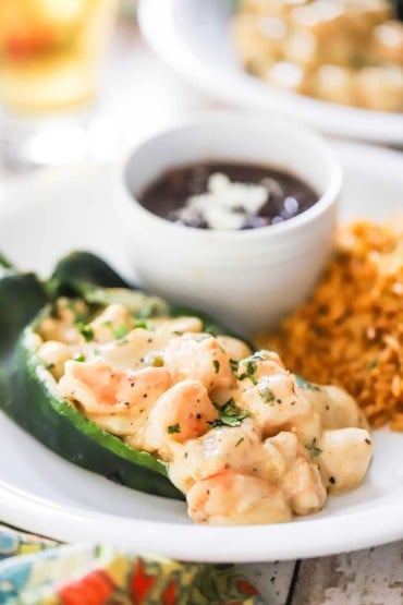 A close-up view of a seafood stuffed poblano pepper on a plate next to Spanish rice and a bowl of black beans.