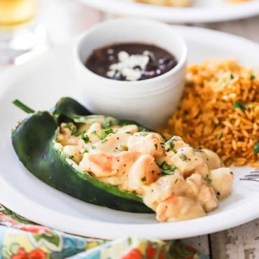 A close-up view of a seafood stuffed poblano pepper on a plate next to Spanish rice and a bowl of black beans.