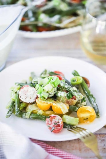 A white salad plate filled with a serving of green bean and tomato salad with scallion dressing.