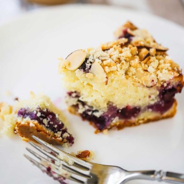 A close-up view of a slice of blueberry coffee cake on a dessert plate with a bite taken out of it.