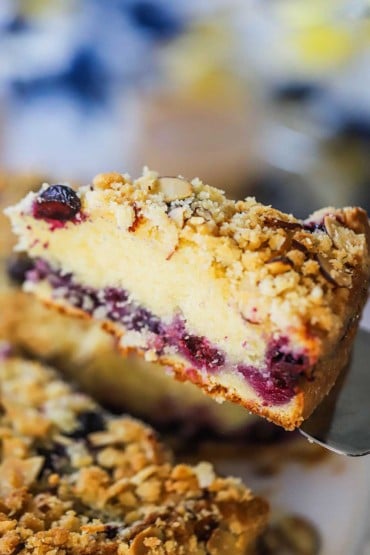 A slice of blueberry almond coffee cake being lifted up with a metal pie spatula.