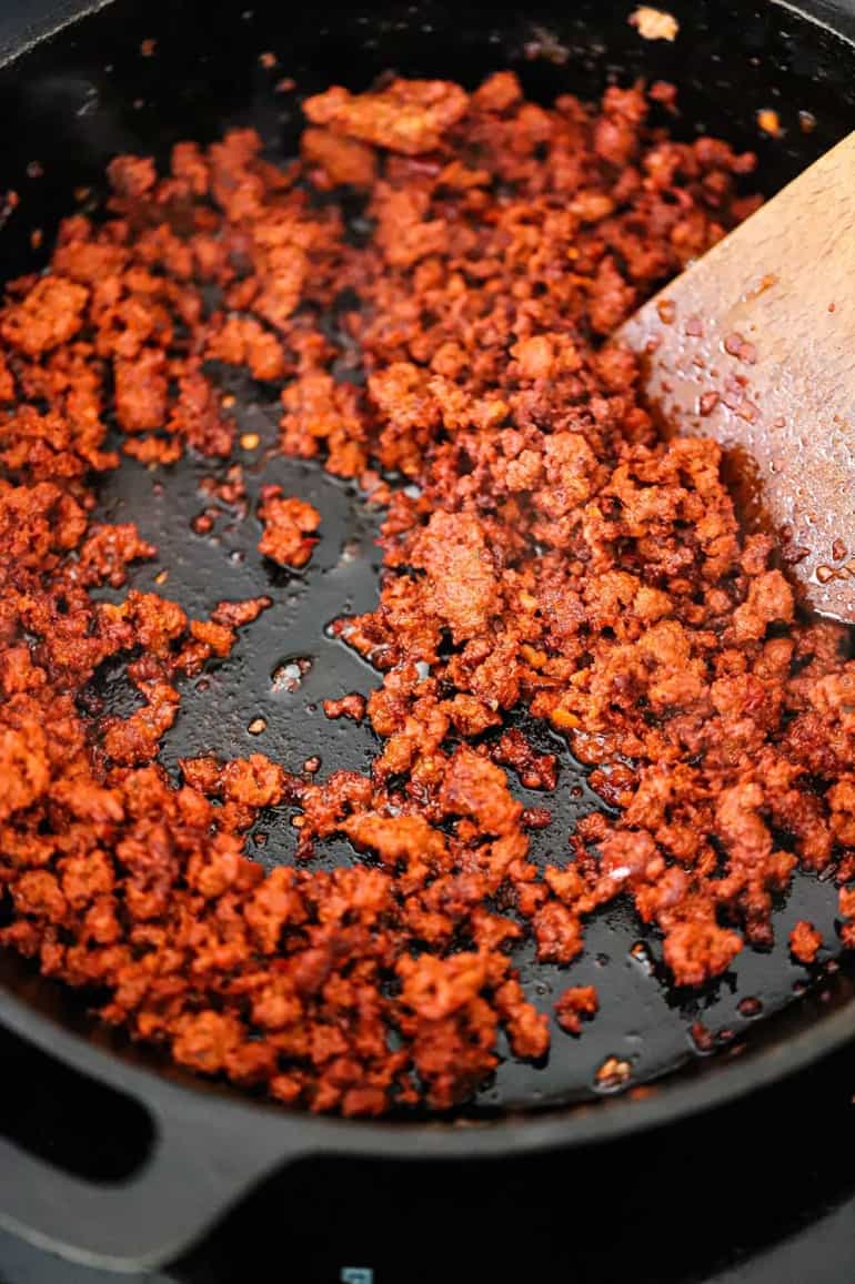 An overhead view of a black cast-iron skillet filled with crumbled cooked chorizo sausage.