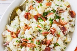 An overhead view of an oval serving bowl filled with creamy horseradish potato salad.