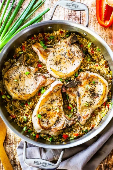 An overhead view of four pan-seared bone-in pork chops sitting in a large skillet of Spanish-style rice.