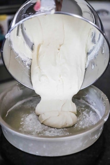 Coffee cake batter being poured from a stand-mixer bowl into a greased and floured cake pan.