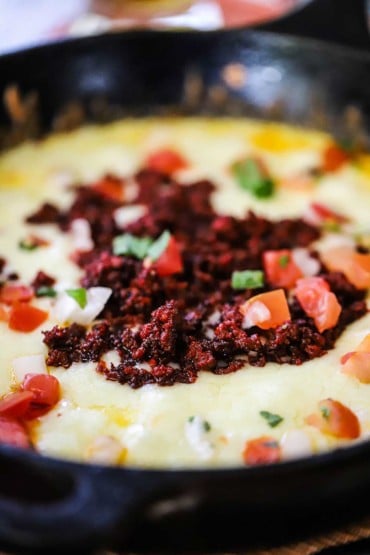 A close-up view of a cast-iron skillet filled with queso fundido garnished with pico de gallo on top.