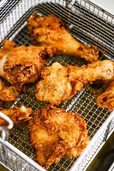 Chicken pieces that have been deep-fried sitting in a basket over the fryer.