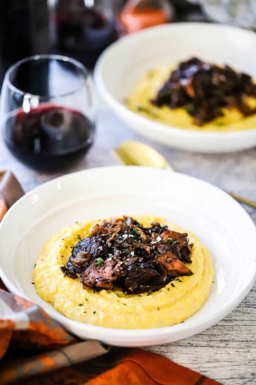 Two white bowls side by side each filled with creamy polenta and caramelized onions and wild mushrooms.