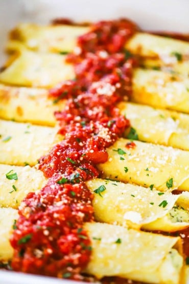A close-up view of a row of cheese stuffed manicotti with a strip of marinara on top.
