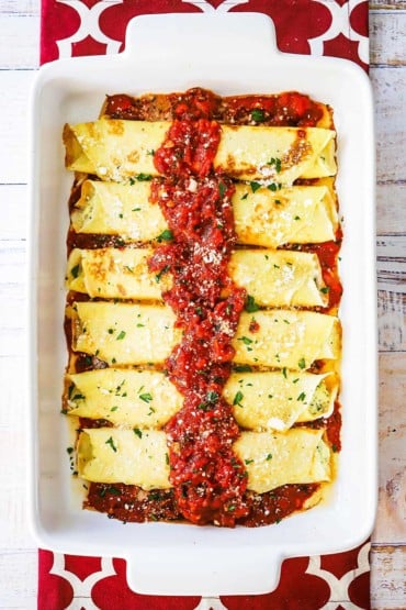 An overhead view of homemade stuffed manicotti in a large white casserole dish and topped with marinara sauce.