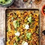 A large rectangular sheet pan piled high with nachos topped with dollops of guacamole and sour cream.