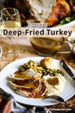A white dinner plate filled with sliced turkey, mashed potatoes, green beans, and gravy next to a glass of white wine and a platter of cooked turkey.