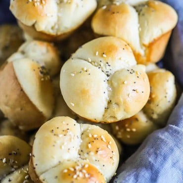 A close-up view of a freshly bake cloverleaf dinner roll sitting in a basket with more rolls.