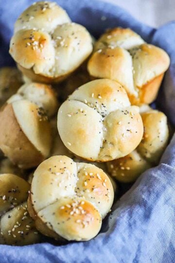 A close-up view of a basket lined with a blue cloth and filled with cloverleaf dinner rolls.