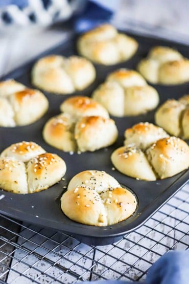 A muffin pan filled with freshly baked cloverleaf dinner rolls sitting on a wire baking rack.