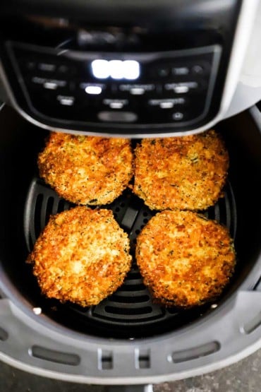 An overhead view of four eggplant medallions that have been breaded and air fried and are sitting in the air fryer basket. 