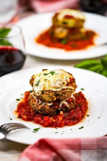 Air fryer eggplant parmesan that is two stacked breaded and fried eggplant circles topped with cheese and on a small pool of marinara sauce on a white plate.