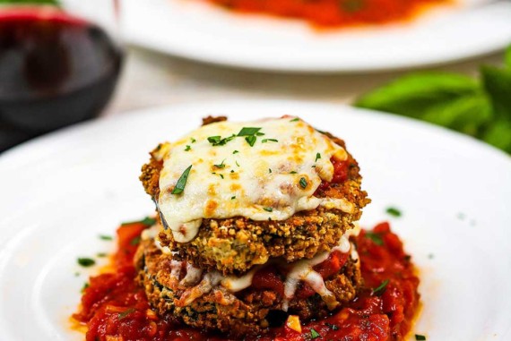 Air fryer eggplant parmesan that is two stacked breaded and fried eggplant circles topped with cheese and on a small pool of marinara sauce on a white plate.