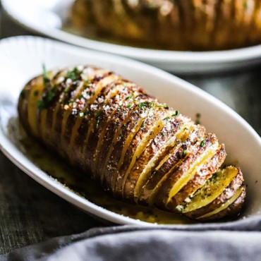 A close-up view of a Hasselback potato sitting in an individual white serving dish.