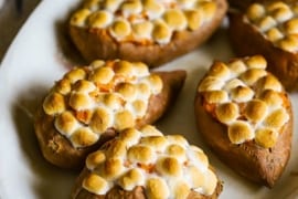A large oval platter holding five twice baked sweet potatoes that are topped with toasted marshmallows