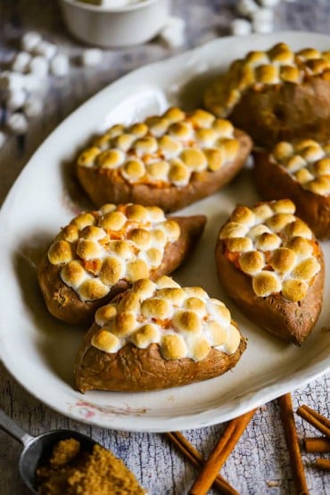 A large oval platter holding five twice baked sweet potatoes that are topped with toasted marshmallows