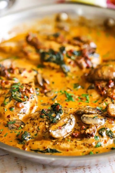 A close-up view of a skillet filled with creamy Tuscan chicken with mushrooms and spinach.