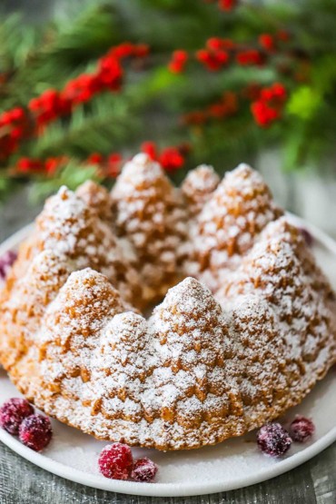 A Christmas bundt cake on a circular cake dish with sugar-coated cranberries around it.