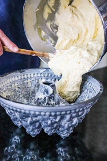 A person using a spatula to transfer almond cake batter into a Christmas bundt pan.