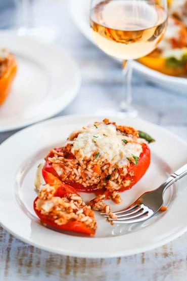 A turkey and rice stuffed bell pepper that has been cut open on a white plate sitting next to a glass of wine.