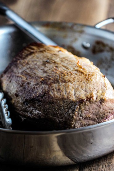 A large rump roast that has been seared and is sitting in a large stainless steel skillet.