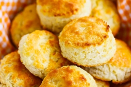 A basket that is lined with an orange checkered cloth and is filled with freshly baked Southern biscuits.