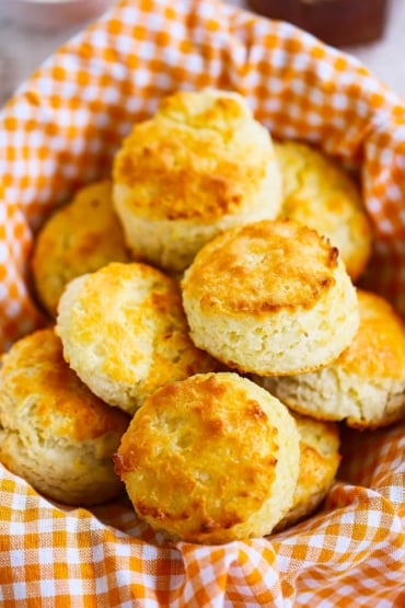 A basket that is lined with an orange checkered cloth and is filled with freshly baked Southern biscuits.